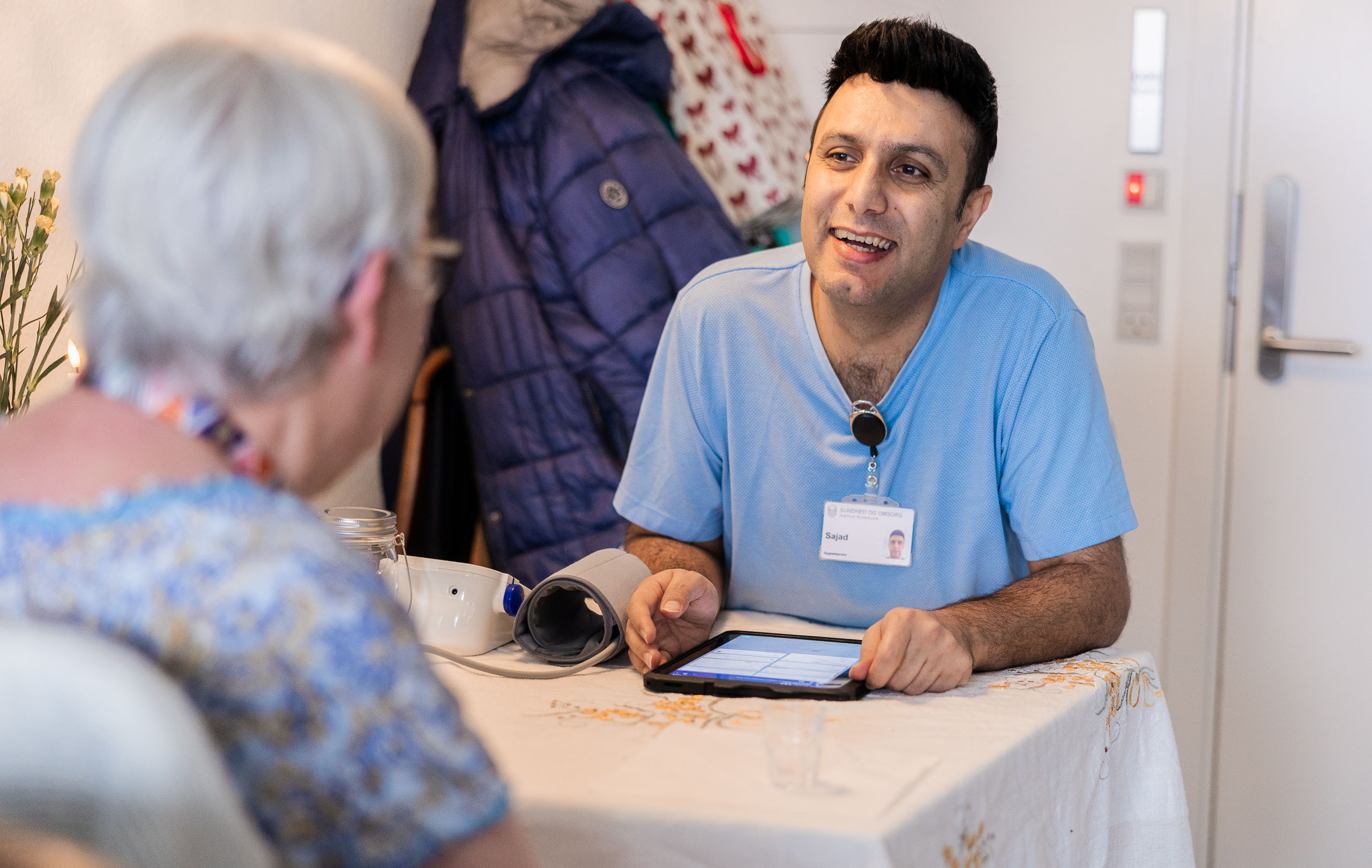 Mandlig sygeplejerske med tablet i hånden snakker med en ældre kvindelig borger